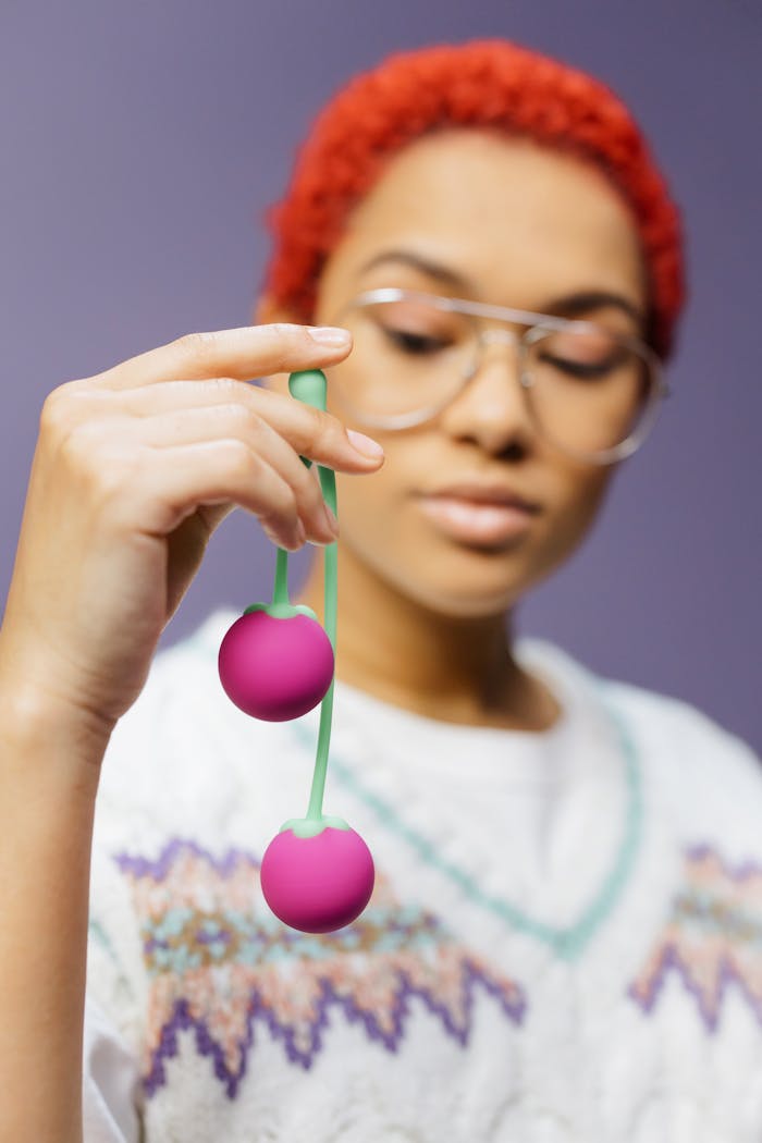 A woman with glasses holds pink kegel balls, emphasizing modern sensuality.