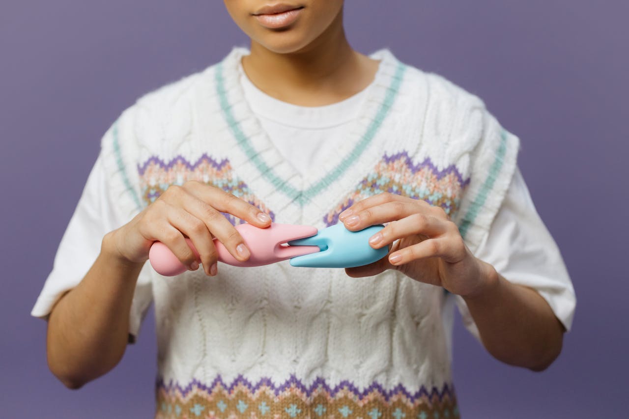 Hands holding pink and blue vibrators against a purple background, highlighting modern intimacy tools.